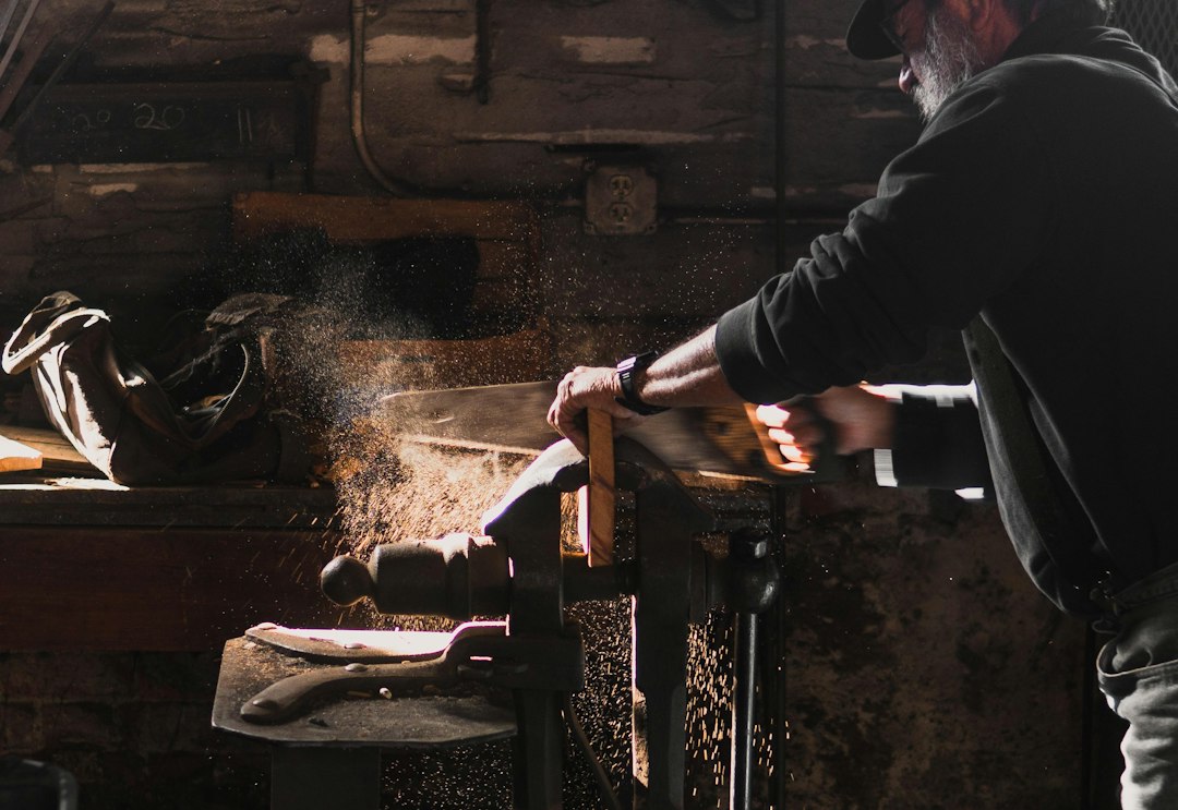 Un artisan en train de scier du bois dans un atelier lumineux, avec des éclats de poussière soulevés par l'action.