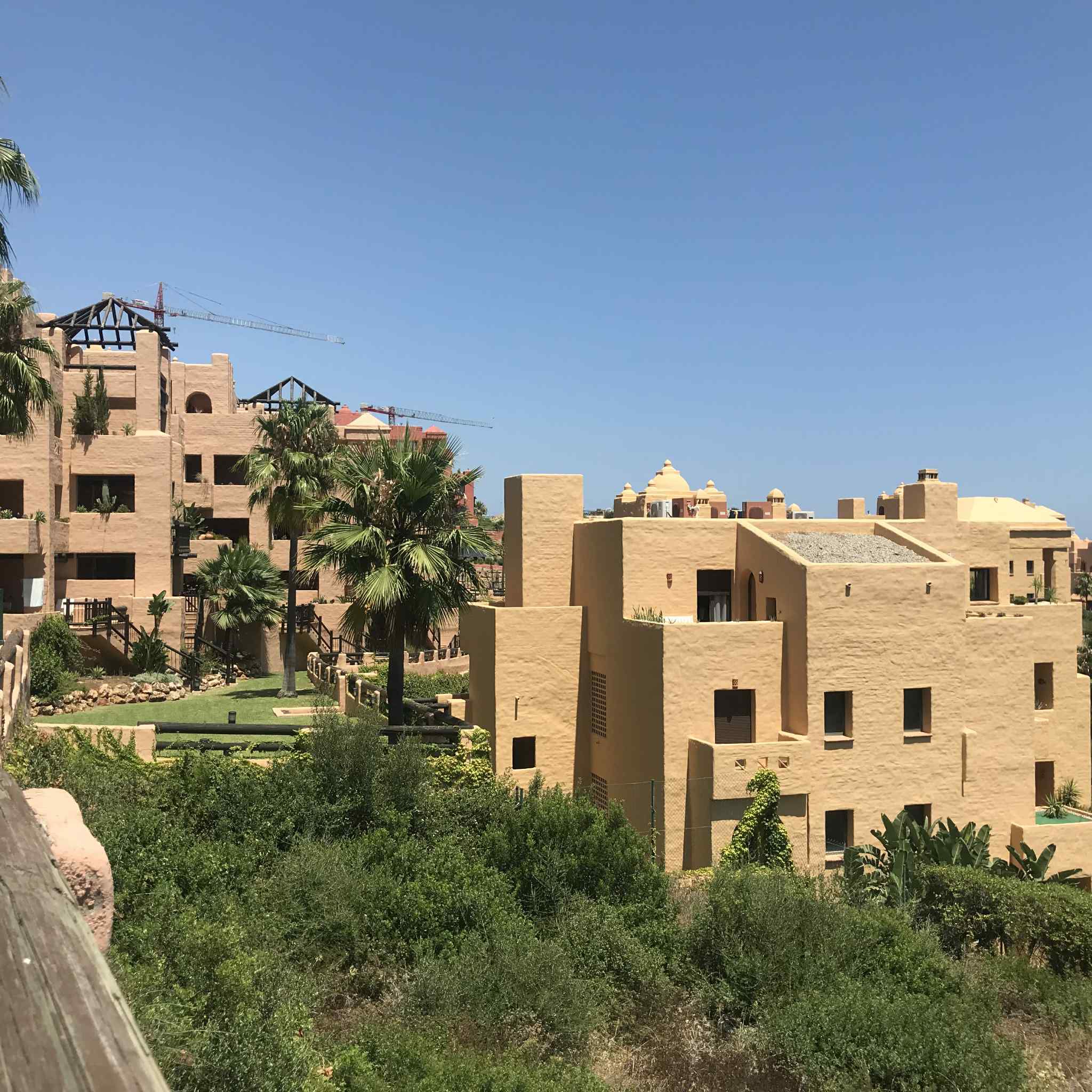 Vue sur des bâtiments modernes au Costa del Sol, entourés de verdure et de palmier, sous un ciel bleu.