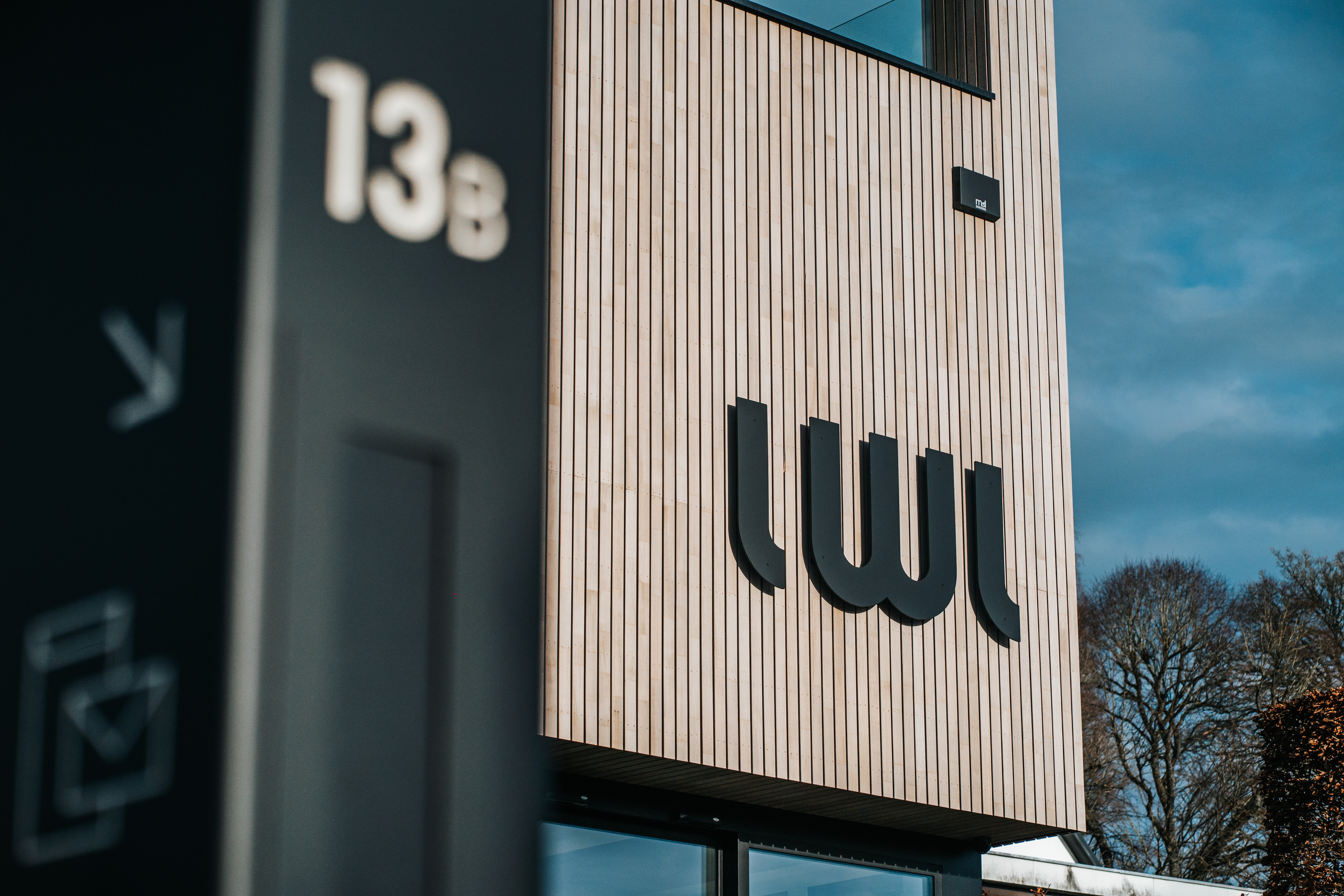 Bureau moderne de LWL Assurances avec une façade en bois et un ciel bleu, situé à Stavelot.