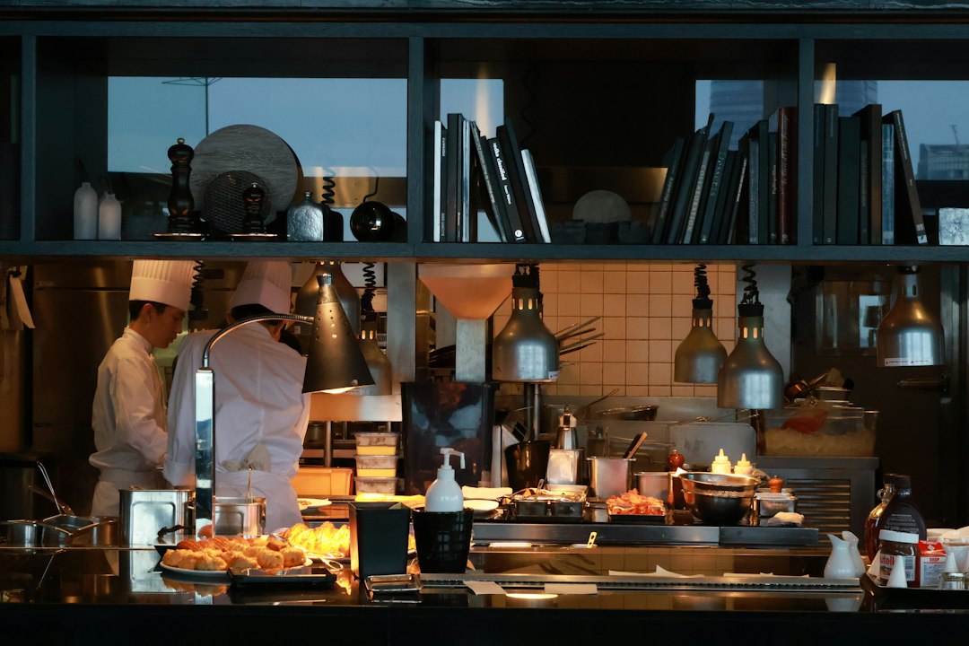Une cuisine moderne avec deux chefs en train de préparer des plats dans un environnement professionnel. Éclairage chaleureux et ambiance dynamique.