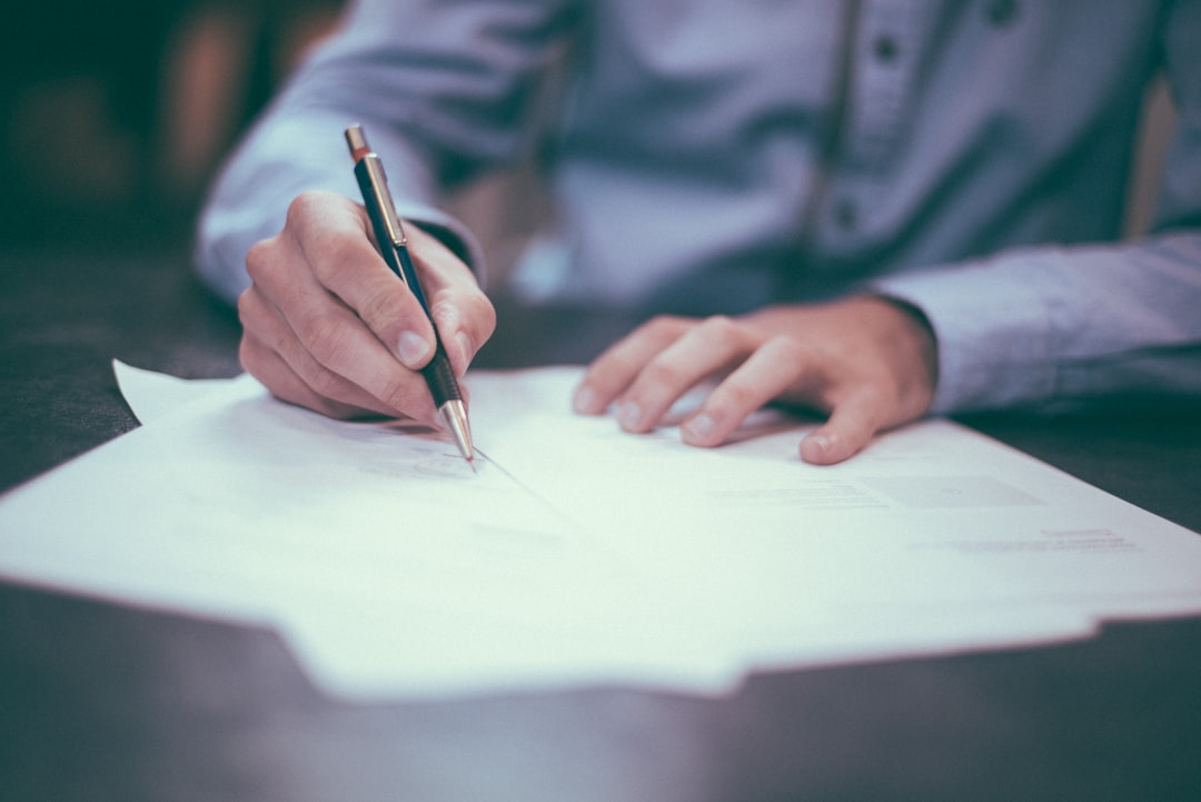 Un homme écrit avec un stylo sur des documents posés sur une table. L'environnement est élégant et professionnel.