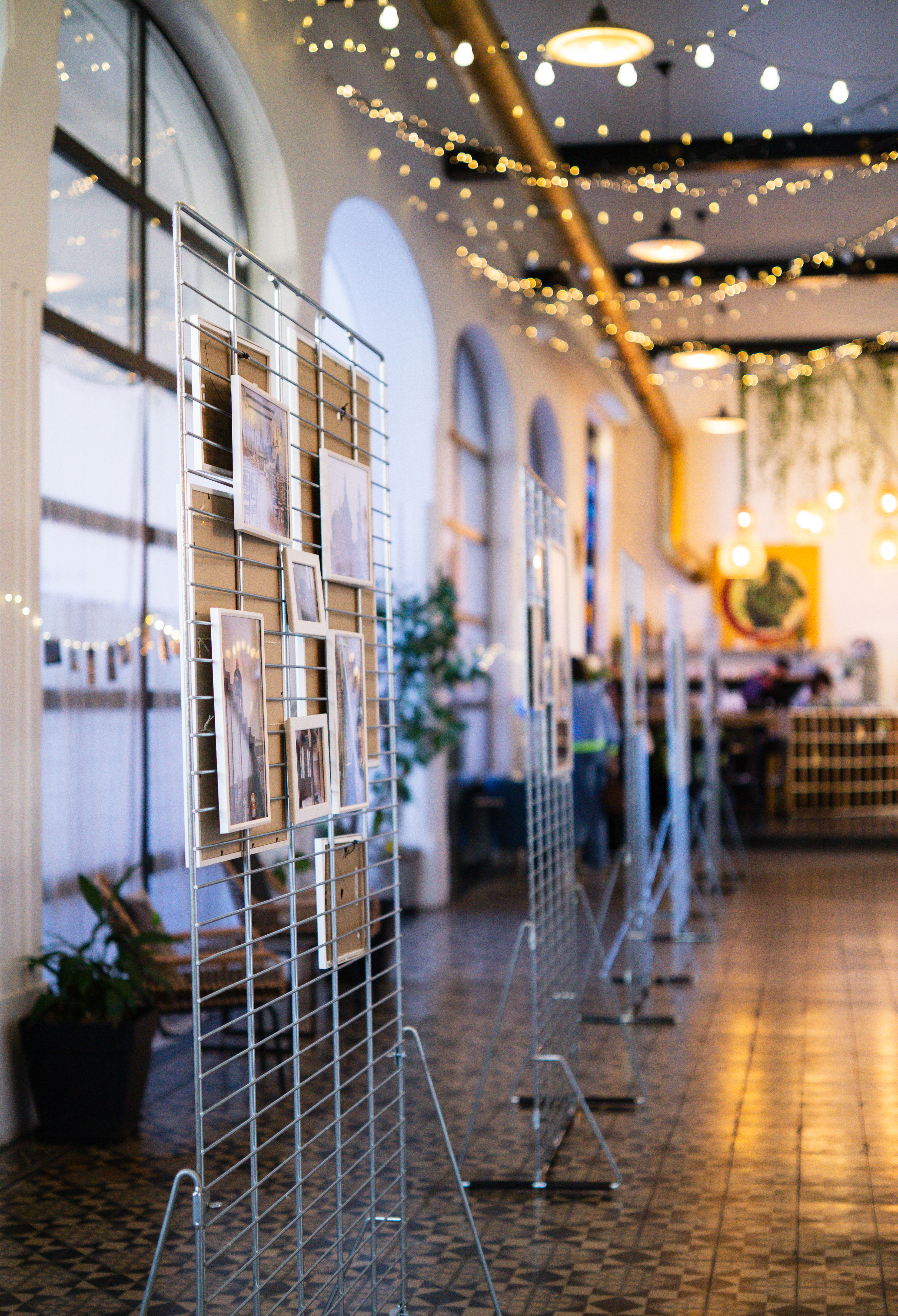Vitrine d'exposition avec des photographies accrochées sur des grilles métalliques dans un espace convivial avec éclairage chaleureux.