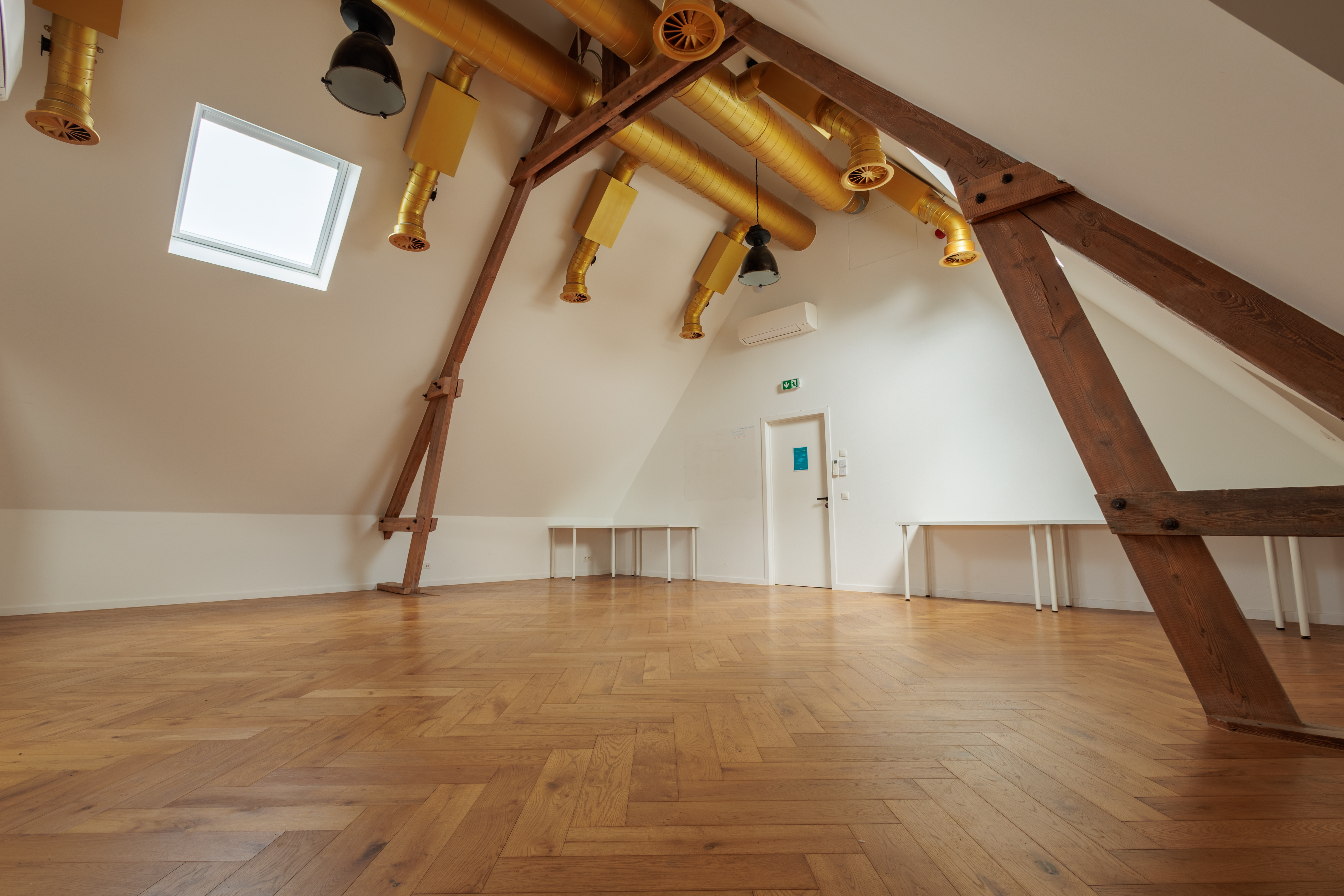 Espace intérieur lumineux avec un parquet en bois et des poutres apparentes, idéal pour des ateliers ou événements à Mons.