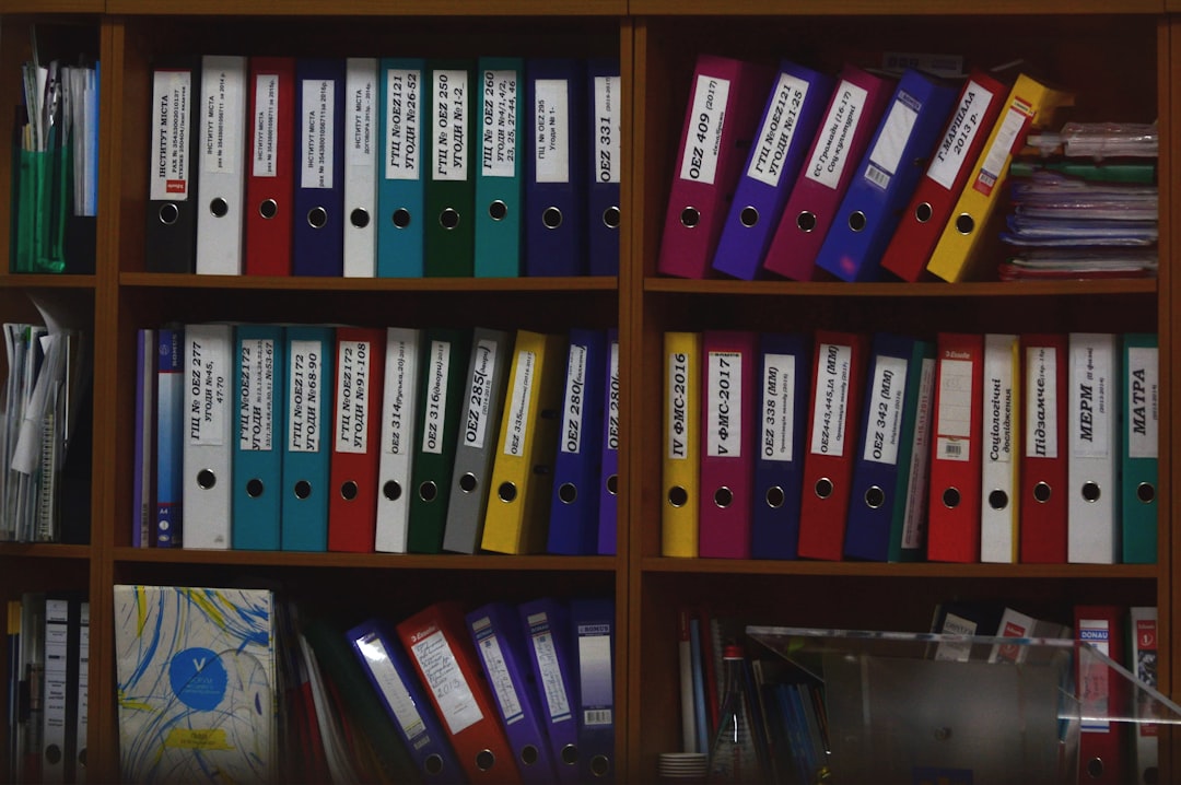 Une étagère remplie de classeurs colorés, organisés de manière ordonnée, entourée de documents et fournitures de bureau.
