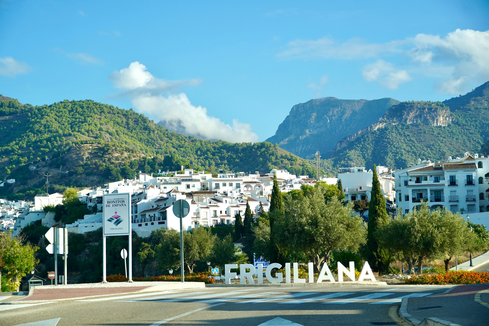 Vue panoramique de Frigiliana avec ses maisons blanches, entourées de montagnes verdoyantes sous un ciel bleu clair.