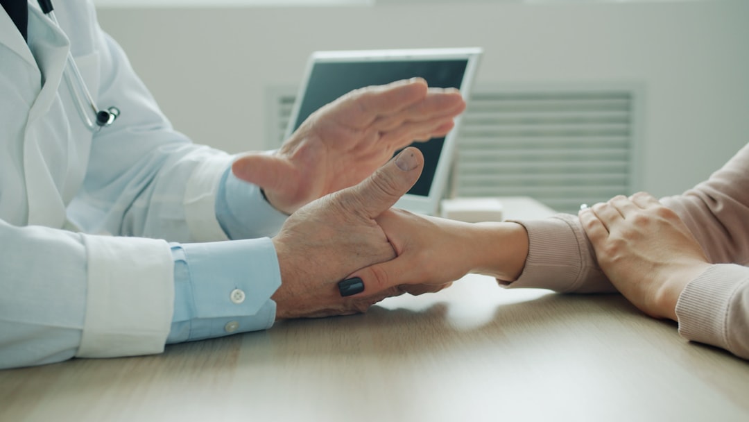 Un médecin en blouse blanche explique quelque chose à un patient en tenant sa main, dans un bureau moderne et lumineux.