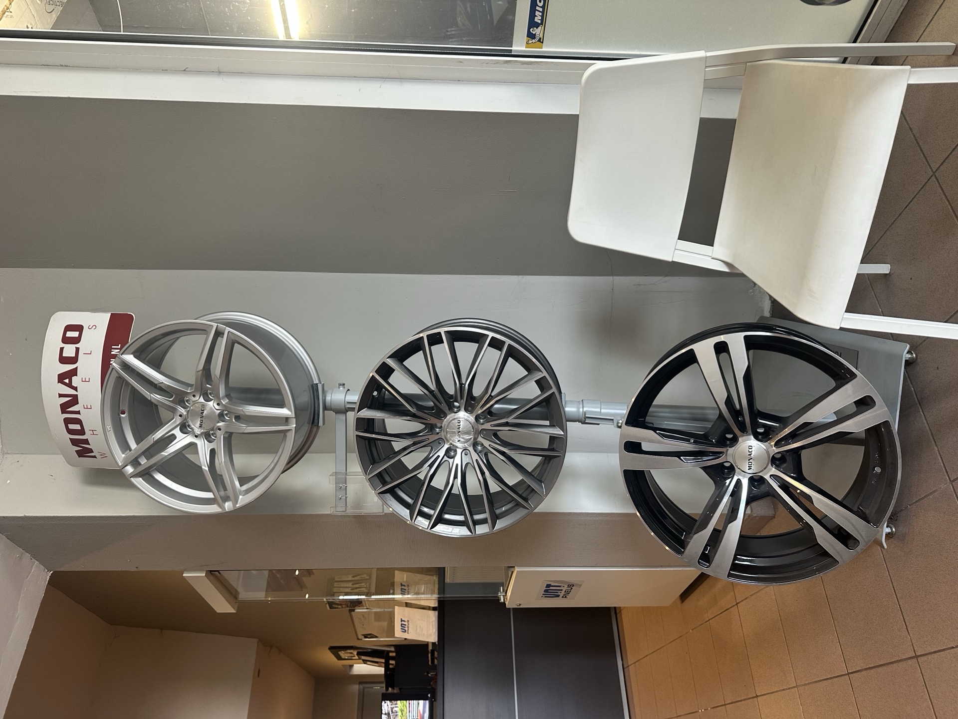 Un présentoir avec trois jantes de voiture brillantes, argentées et noires, dans un espace de vente.
