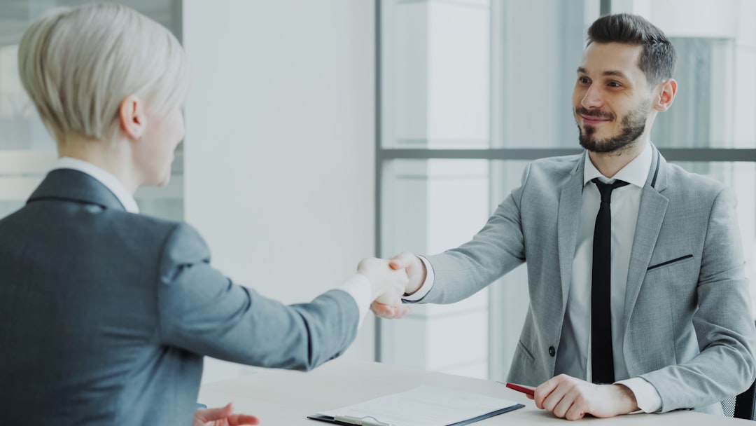 Deux professionnels se serrent la main lors d'une réunion dans un bureau moderne, lumineux. Atmosphère de collaboration et de confiance.