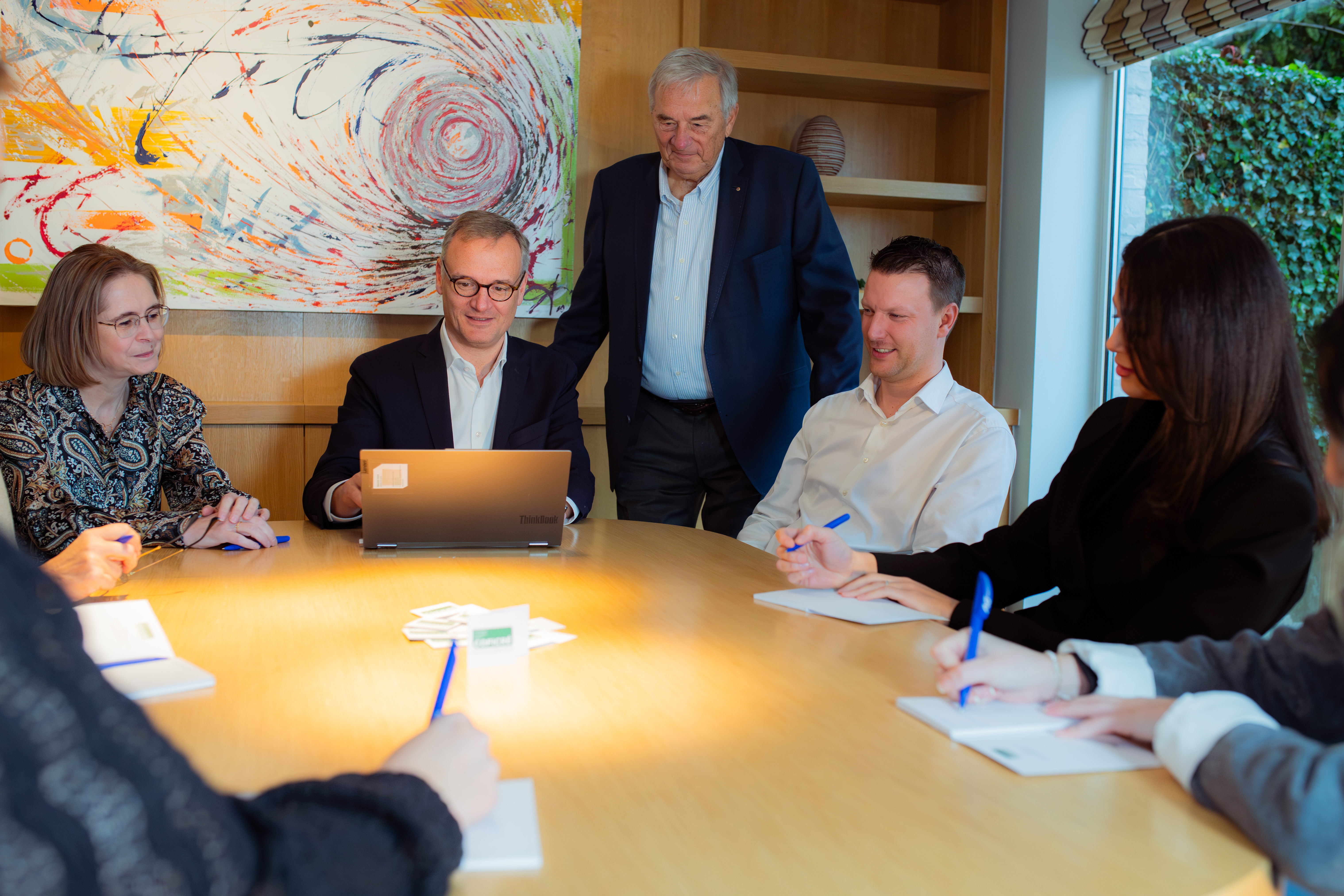 Une réunion autour d'une table avec des professionnels, des ordinateurs portables et des notes, dans un environnement lumineux et moderne.