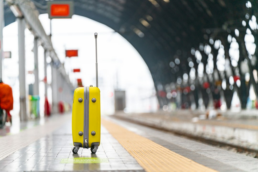 Valise jaune posée sur le quai d'une gare sous une structure architecturale moderne.