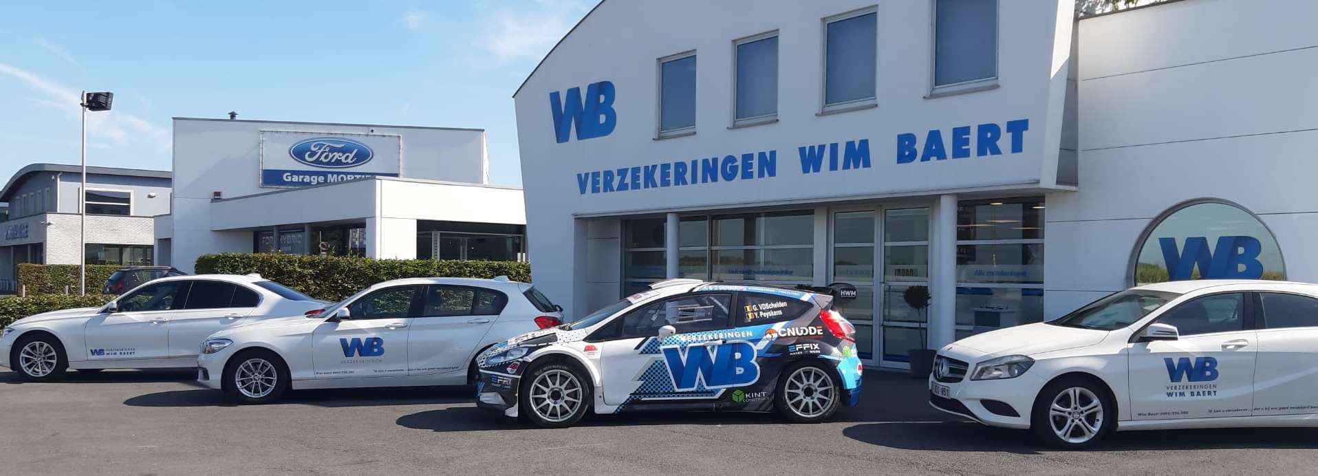 Een parkeerplaats met verschillende auto's en een kantoorgebouw van een verzekeringsbedrijf in de zon.