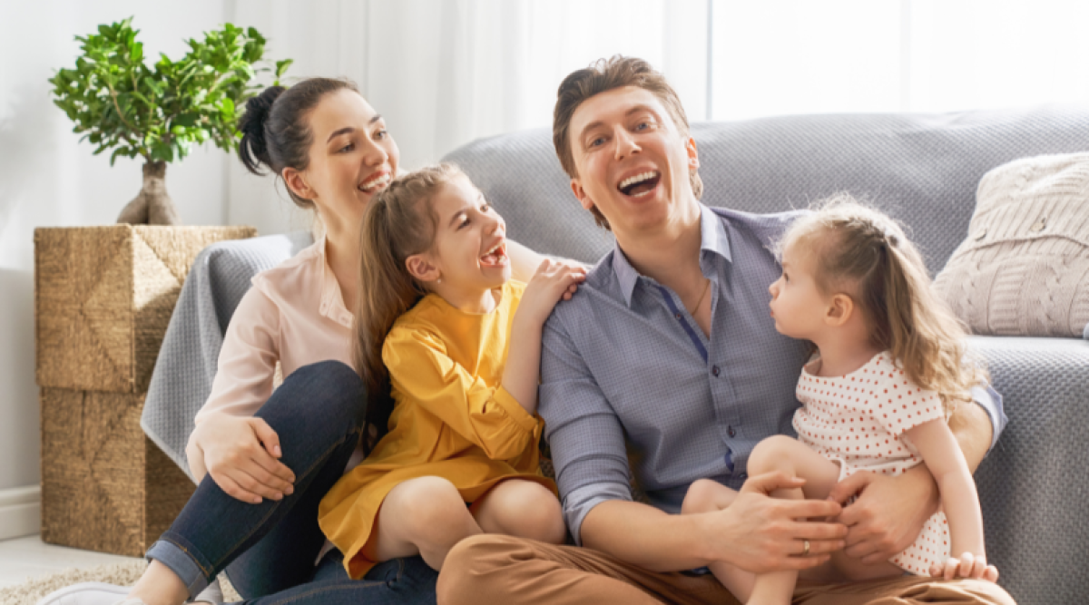 Une famille souriante est assise sur le sol, entourée de rires et de joie, avec deux jeunes filles et leurs parents.