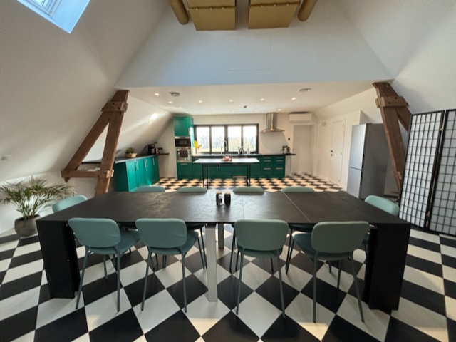 Une cuisine moderne avec un sol en damier noir et blanc, une grande table à manger et des meubles de rangement verts.