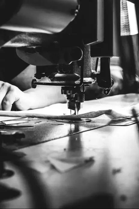 Une main proche d'une machine à coudre, travaillant sur un tissu.